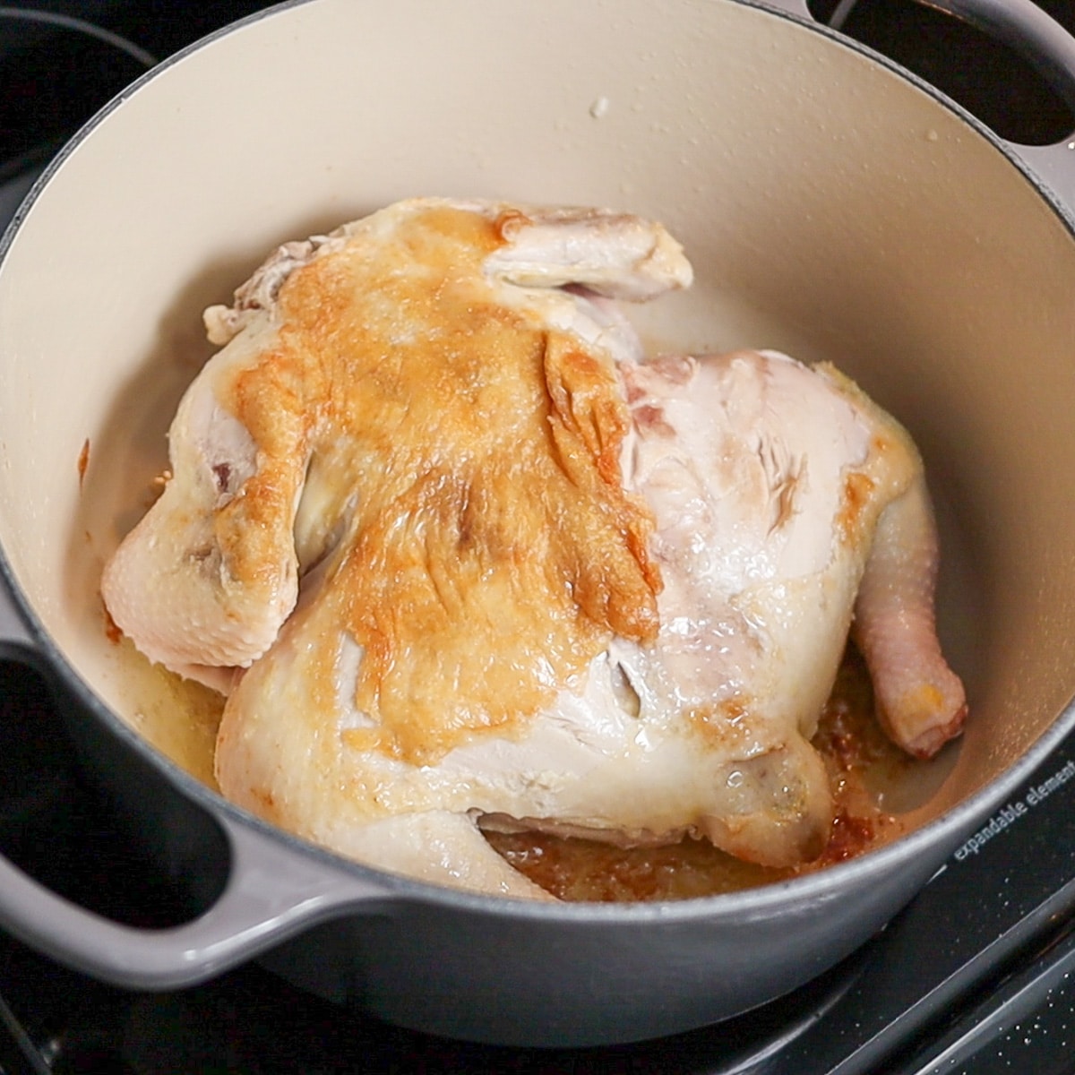 whole chicken browning in a dutch oven
