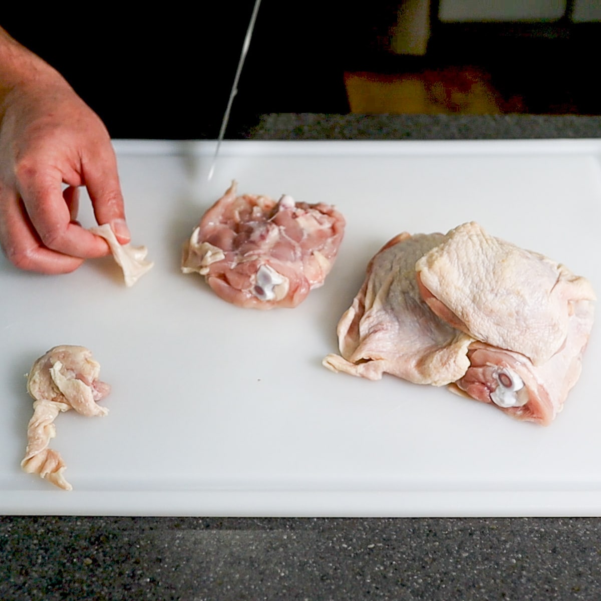 cutting excess the fat off a chicken thigh