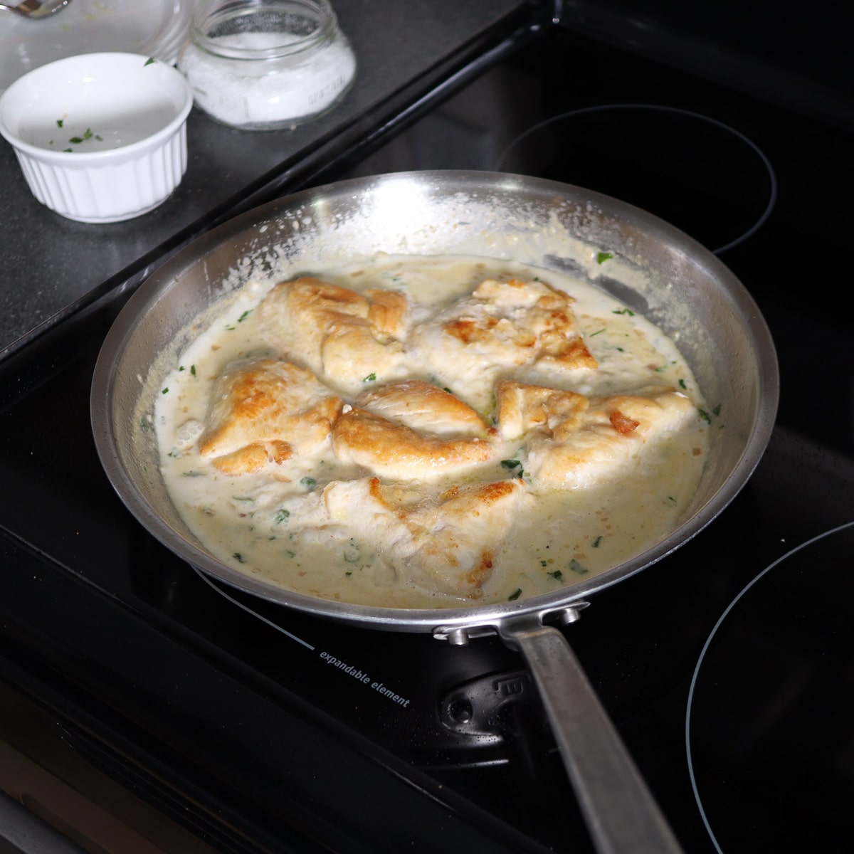 the chicken in a pan with the cream sauce simmering