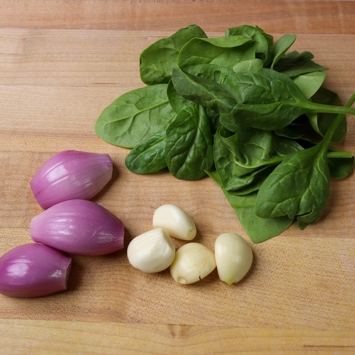 shallots, spinach and garlic on a cutting board
