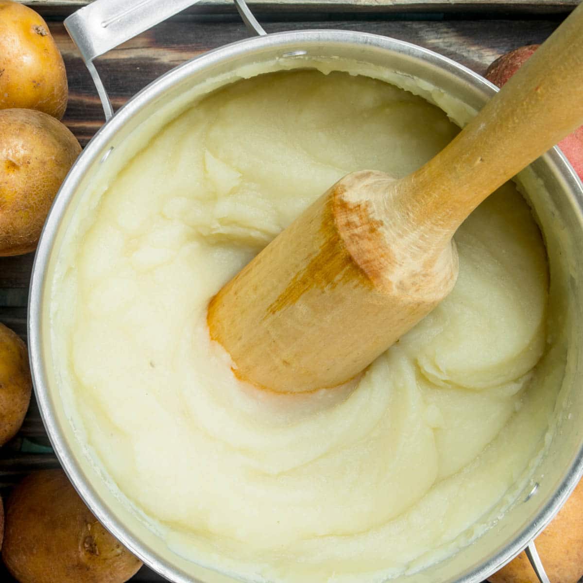 Mashed Potatoes in a pot with a wooden masher.
