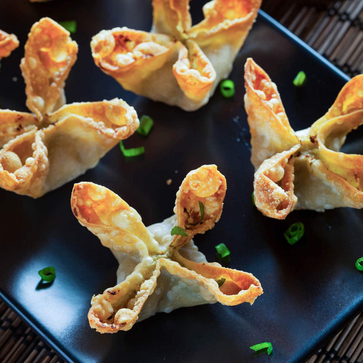 Four Crab Rangoon on a black dish with chopped scallions spread on the dish 