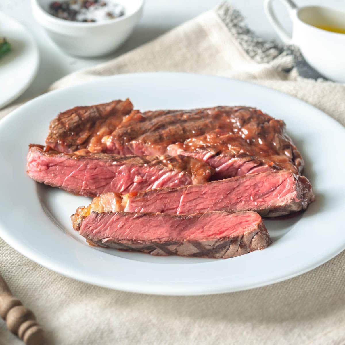 Grilled steak cut into strips on a white plate with a linen place mat underneath.