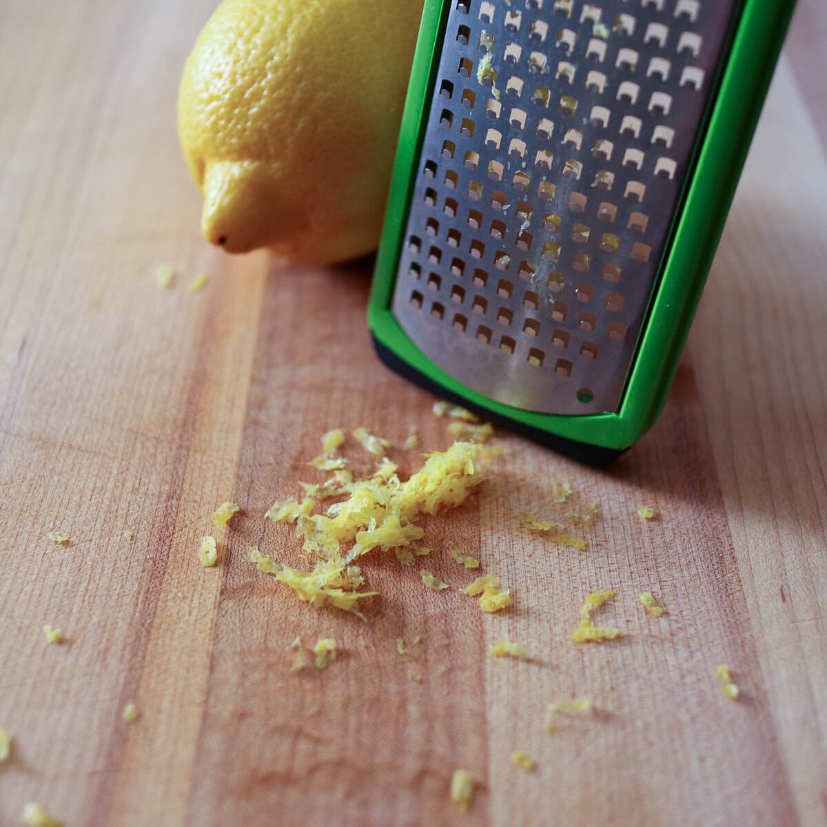 Microplane with a lemon behind and fresh lemon zest in a pile in front.