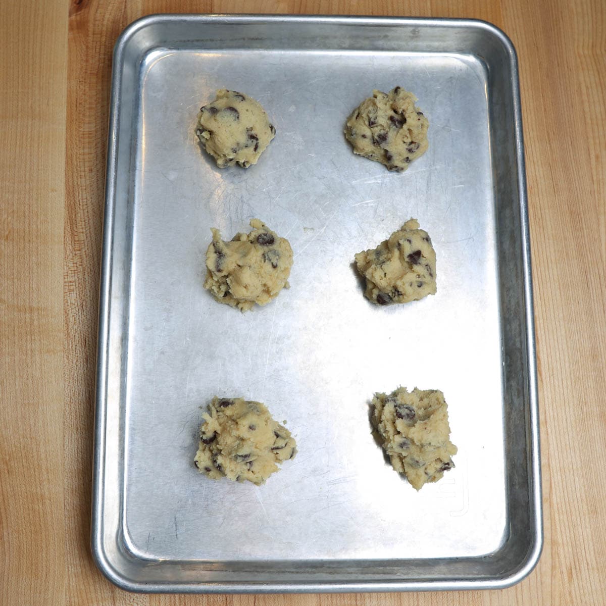 !/2 sheet cookie pan with 6 balls of raw chocolate chip cookie dough.