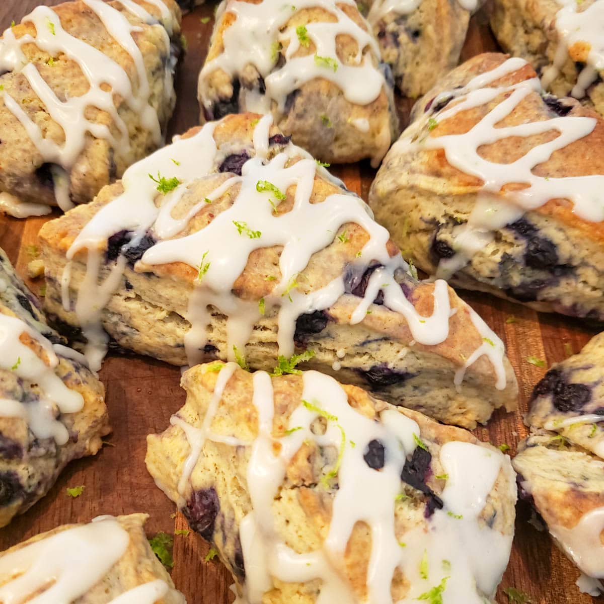 Blueberry lime scones drizzled with icing on a dark cutting board