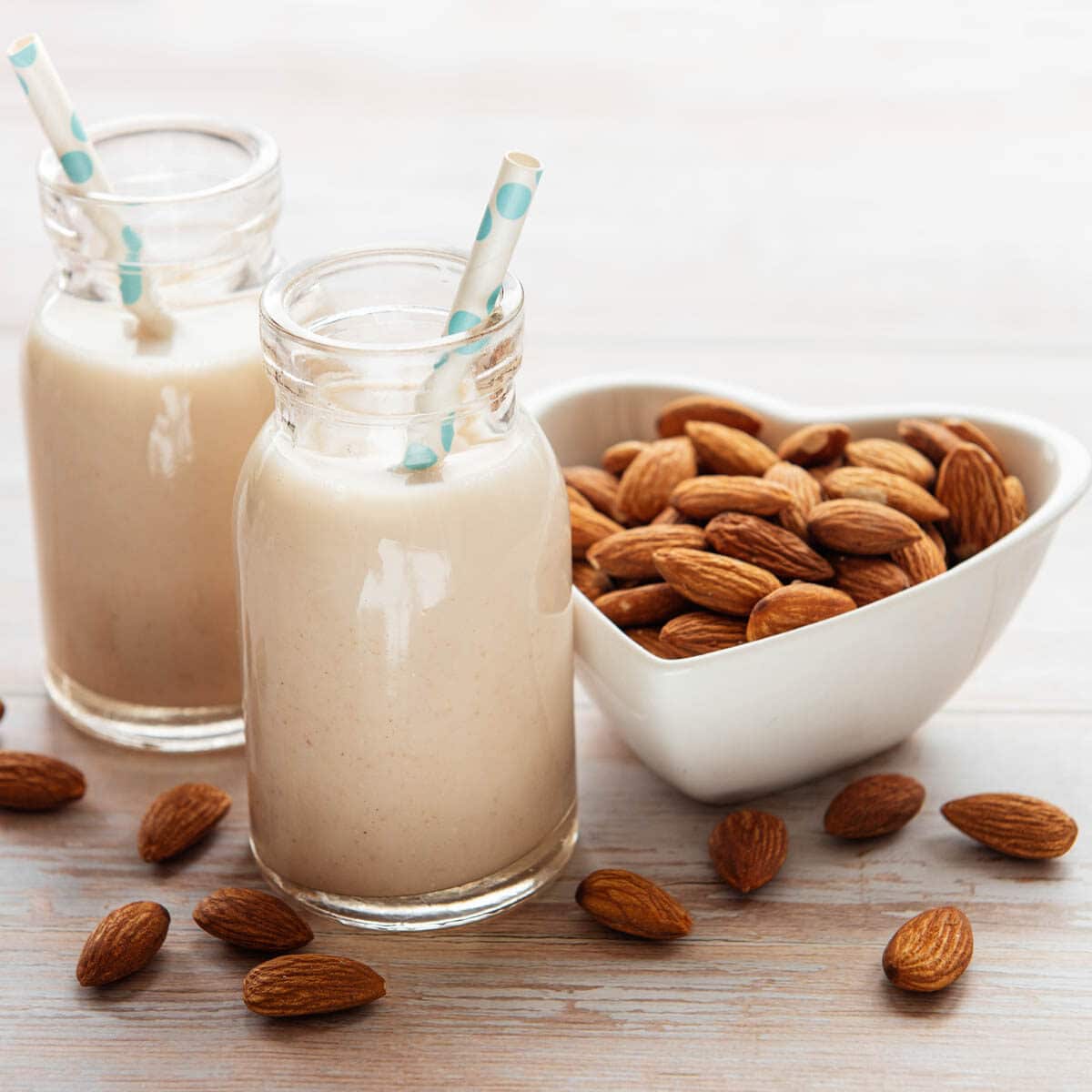 Two small glass jars of almond milk with a heart shaped bowl of almonds next to them.