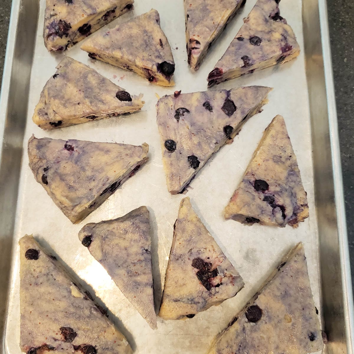Raw scone triangles on a metal baking sheet.