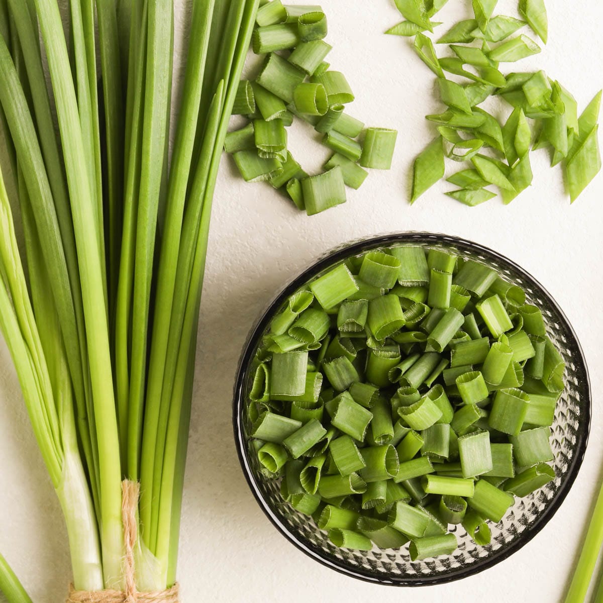 Whole green onions next to bowl of chopped green onions.