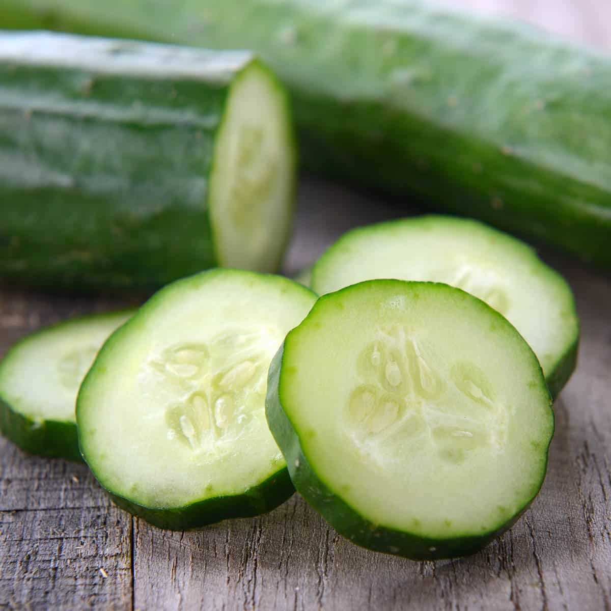 A whole cucumber next to a cut cucumber with slices.