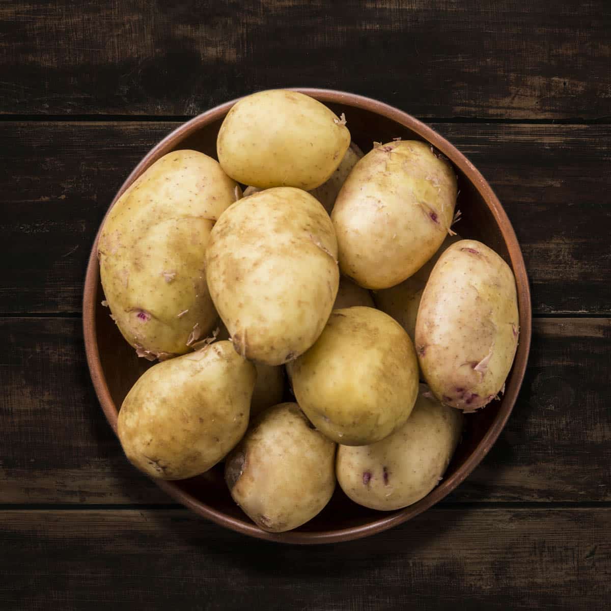 Bowl of raw Yukon potatoes on a dark background