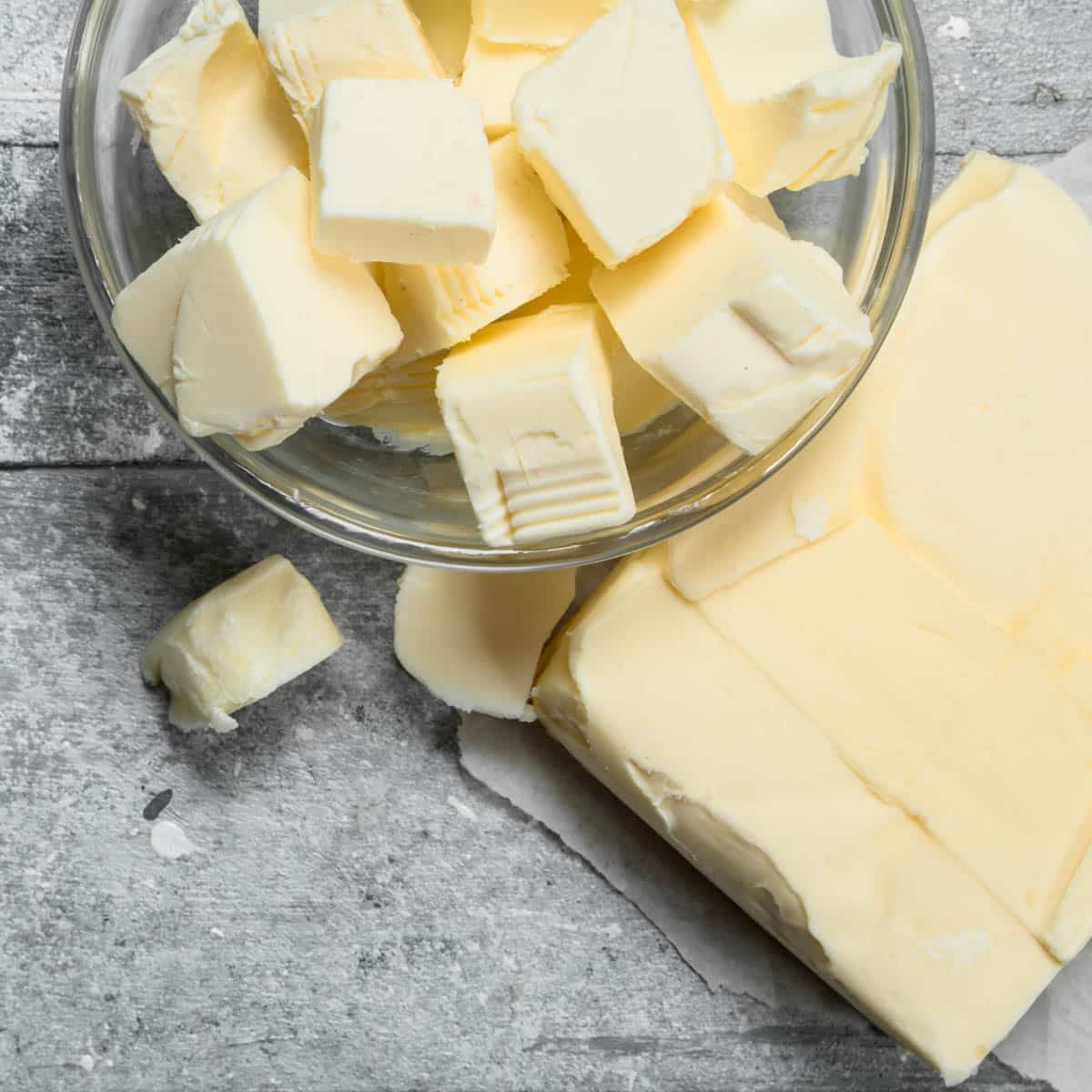 Block of butter next to a glass bowl with cubed butter