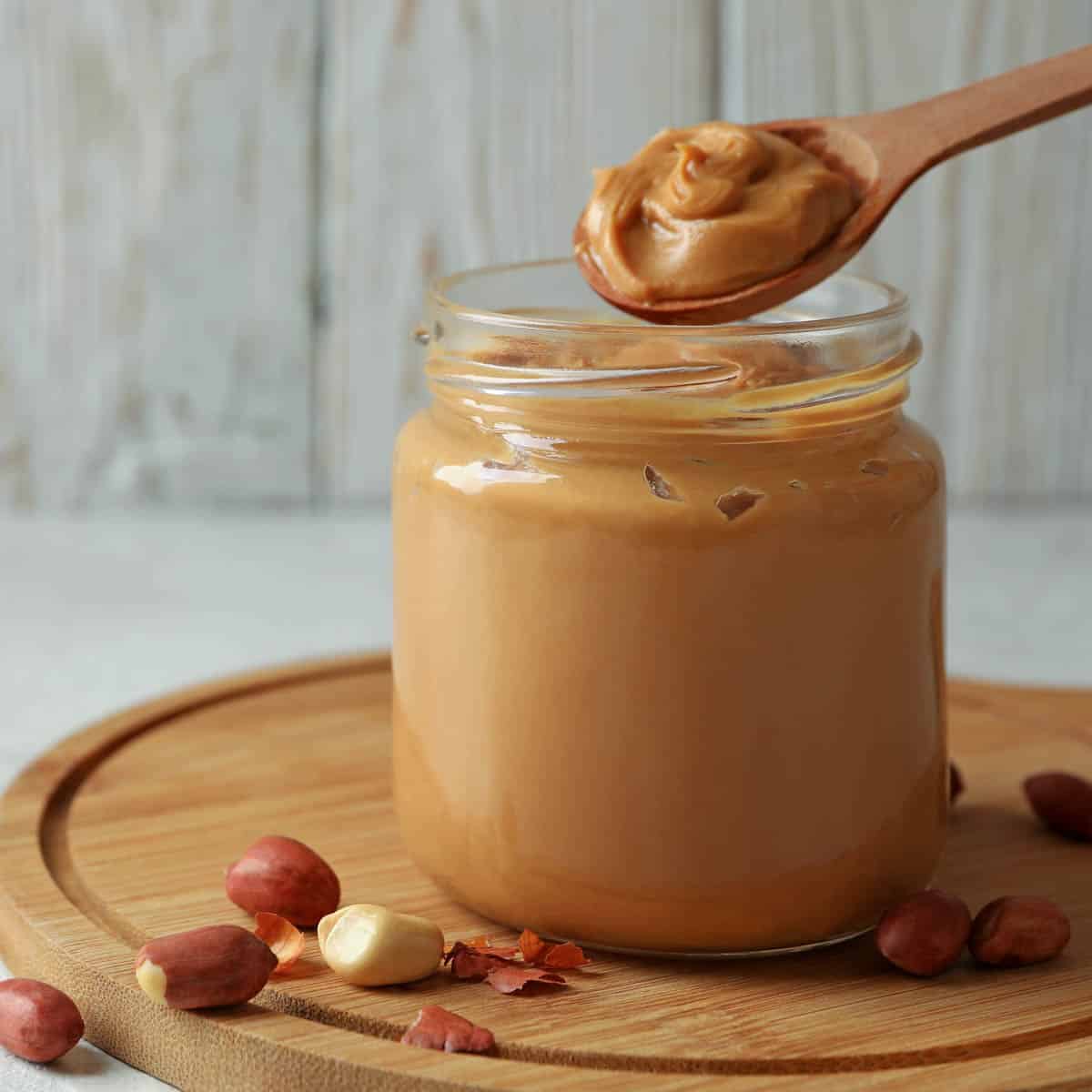 Jar of peanut butter on a round cutting board with a few peanuts on the board.