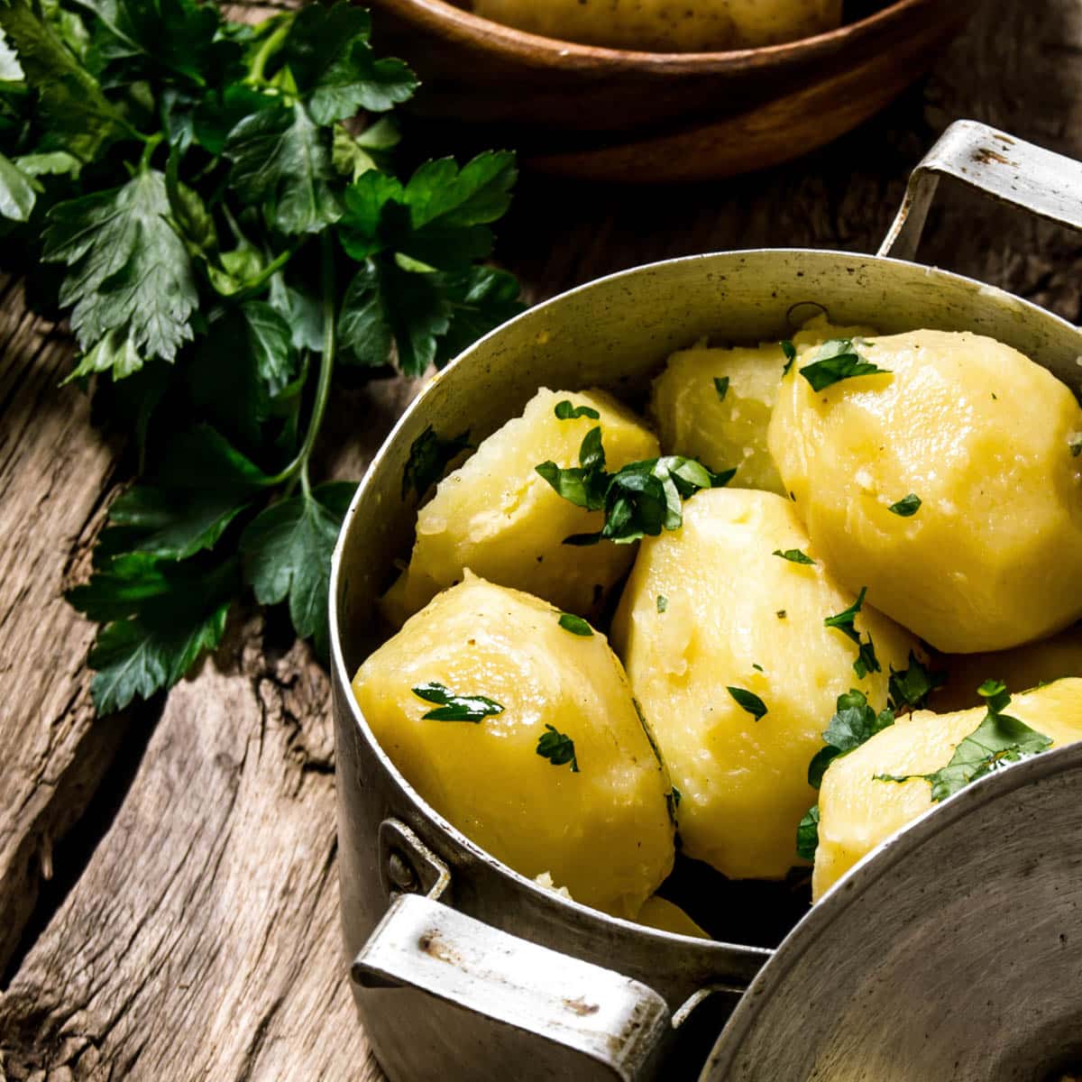Boiled potatoes with fresh herbs in a pot on a rustic wooden table.