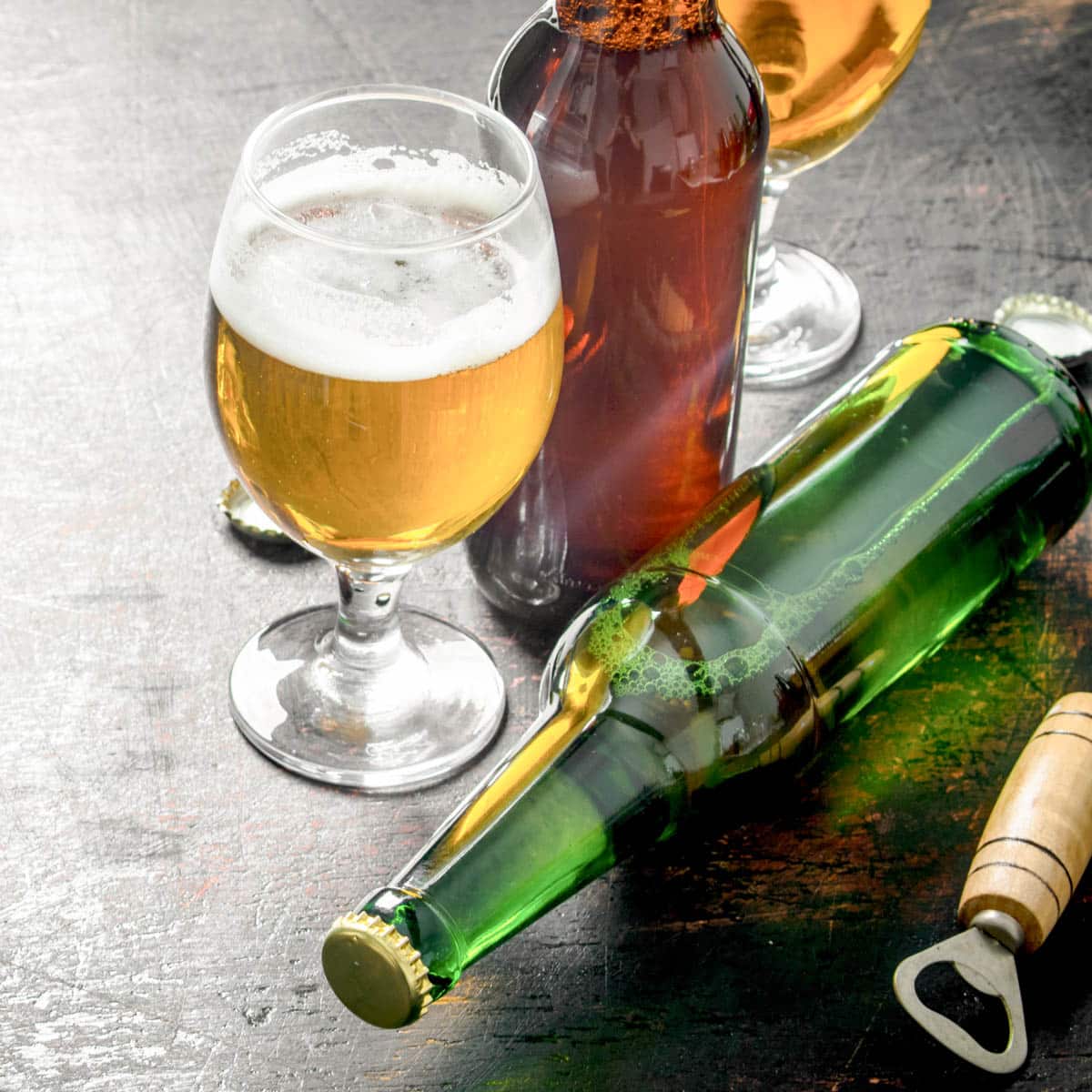 Glass of beer with beer bottles next to it on a rustic background.