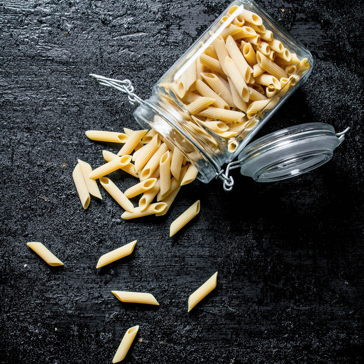 Glass jar with dried pasta spilling out onto a black counter.
