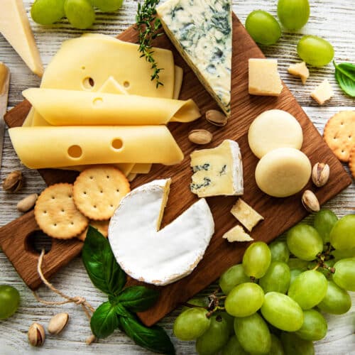 A variety of cheese and crackers along with nuts and grapes on a cutting board.