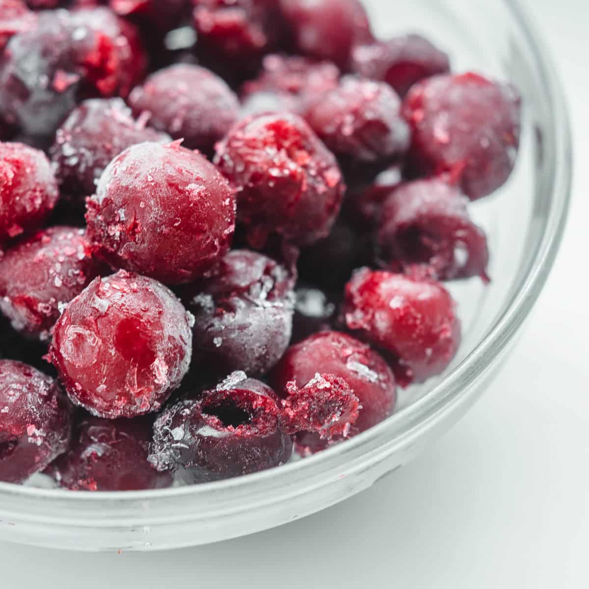 A glass bowl filled with frozen cherries.