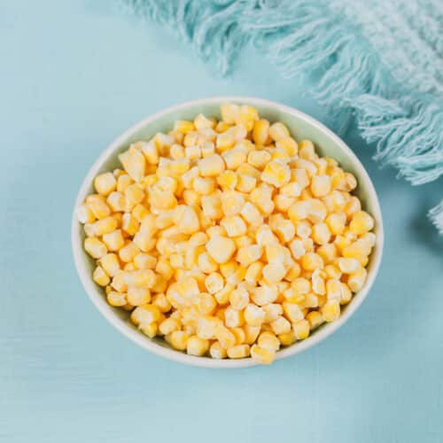 Bowl filled with frozen corn on a blue background.
