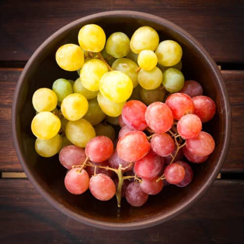 Top view of a wooden bowl filled with green and red grapes.
