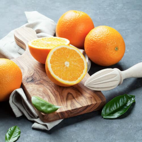 Fresh oranges on a cutting board with a reamer.