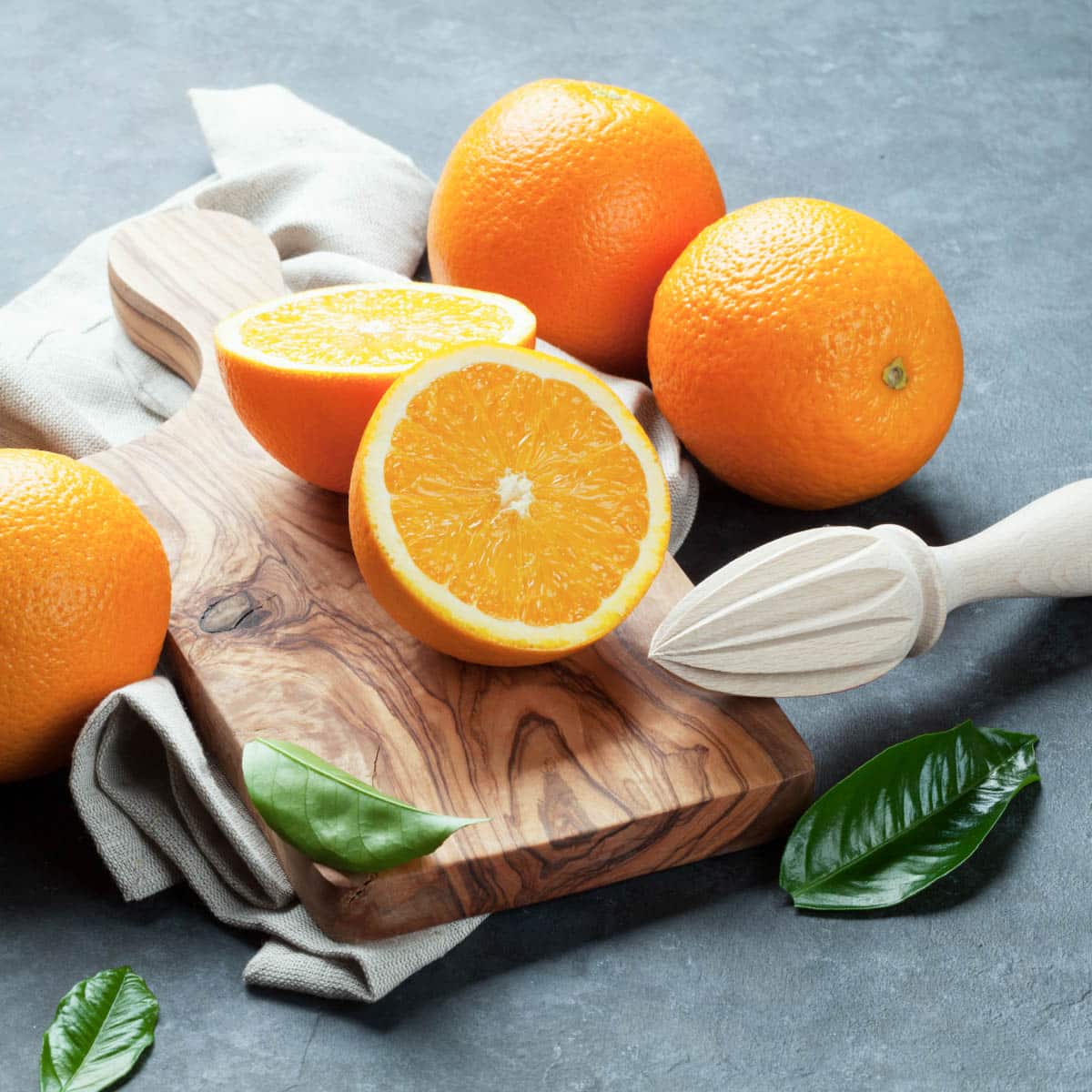 Fresh oranges on a cutting board with a wooden reamer.