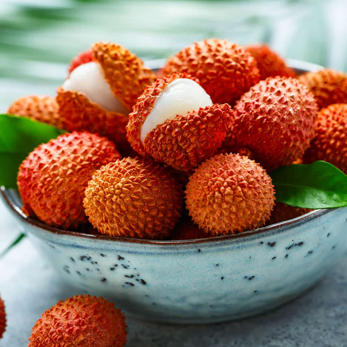 A bowl filled with ripe lychee, some of them cracked in half to show the fruit inside.