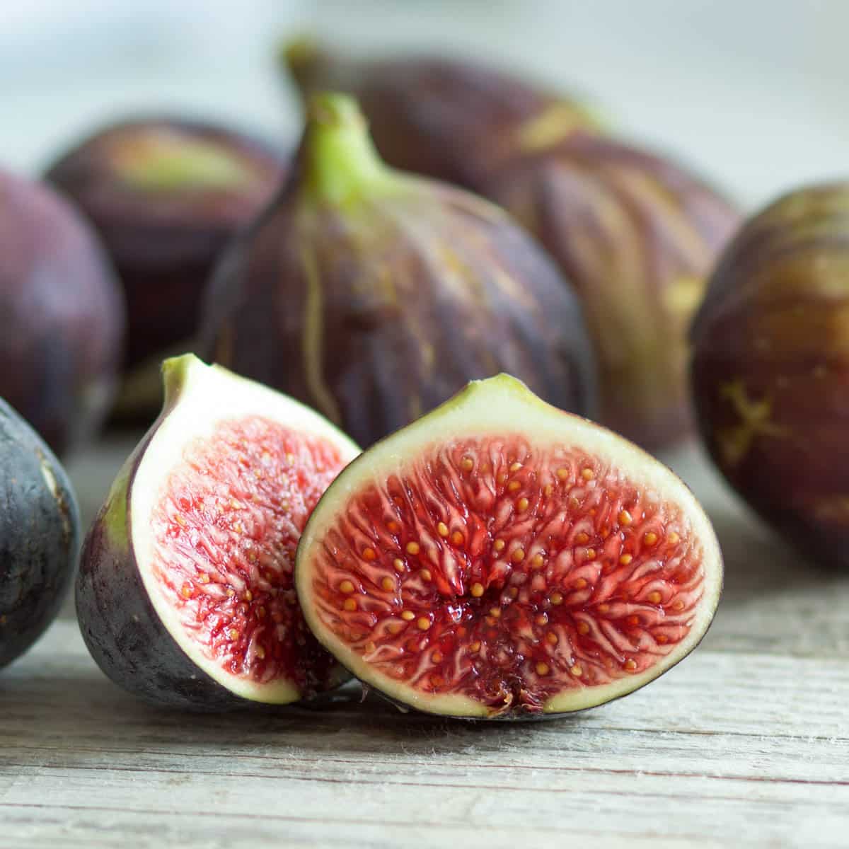 A ripe fig cut in half with other whole figs in the background on a wooden table.