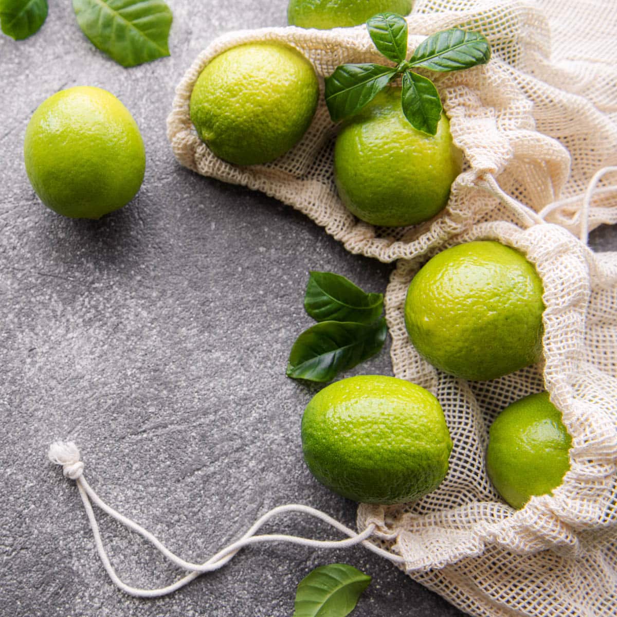 Ripe limes spilling out of a mesh produce bag on a grey counter.