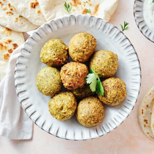 Top view of a white plate with falafel balls surrounded by pitas.