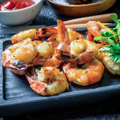 Cooked shrimp on a dark wooden cutting board.