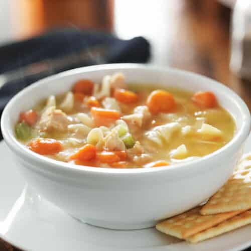 White bowl of homemade chicken noodle soup with crackers.