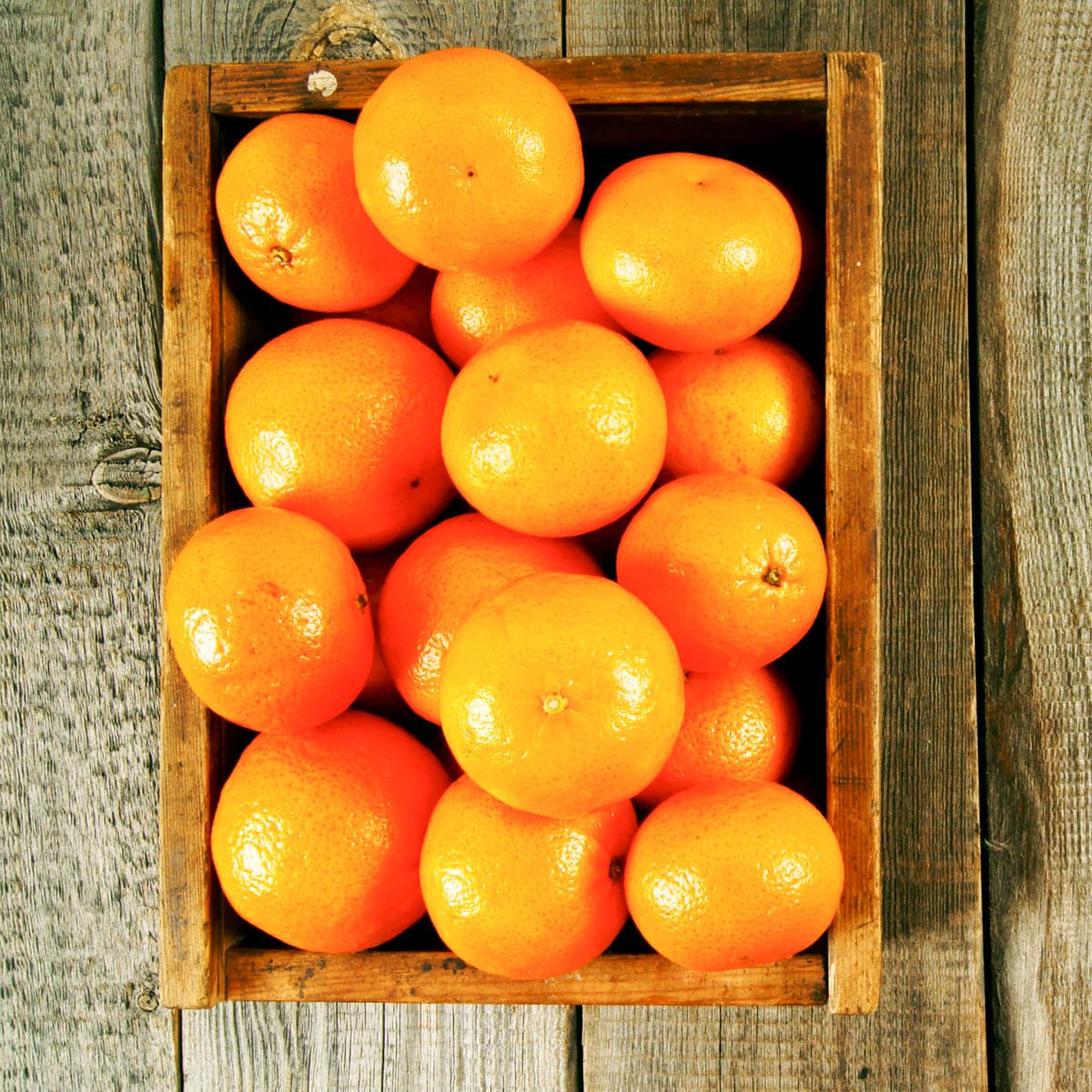 Top view of a wooden box filled with ripe tangerines on a wooden table.