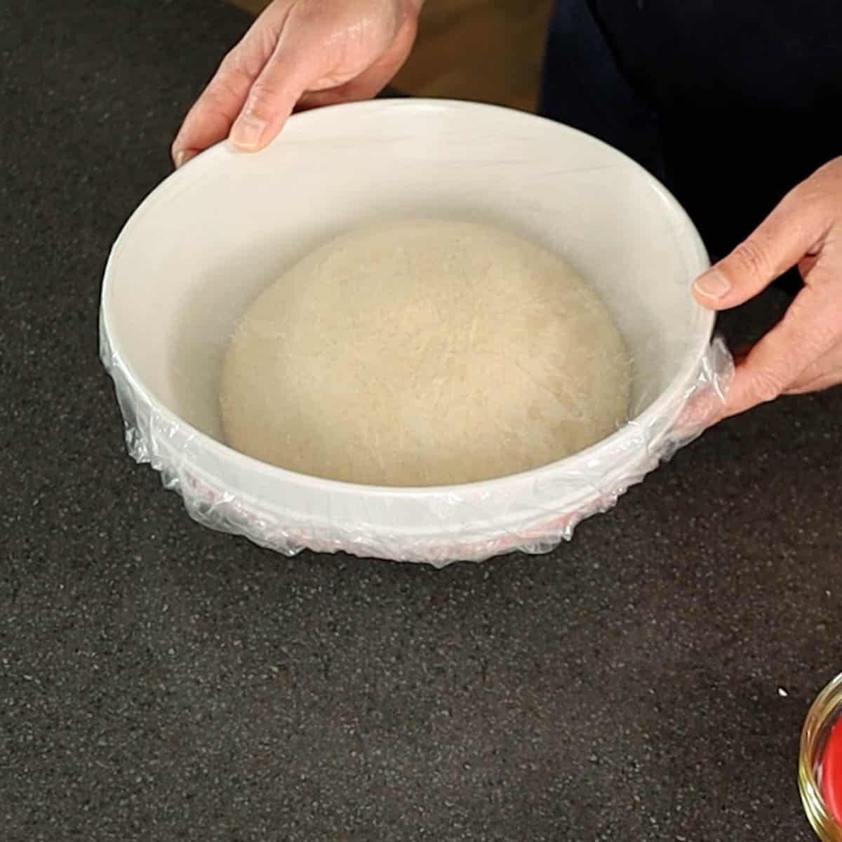Sourdough flatbread dough ball in a white bowl with plastic bonnet proofing.