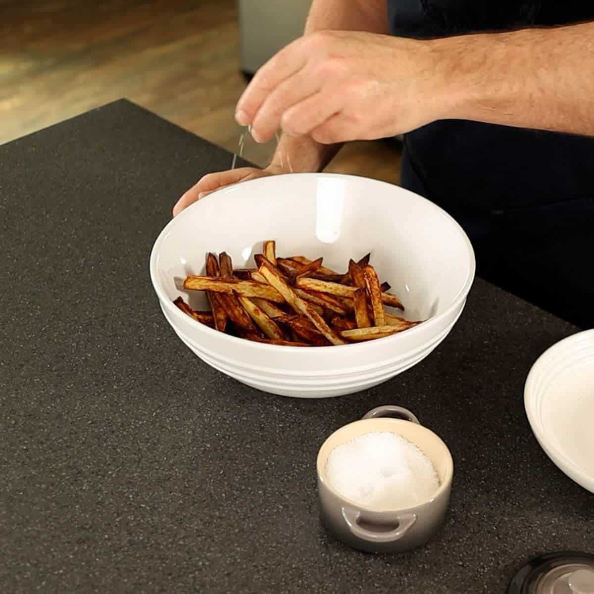 Seasoning French fries in a white mixing bowl